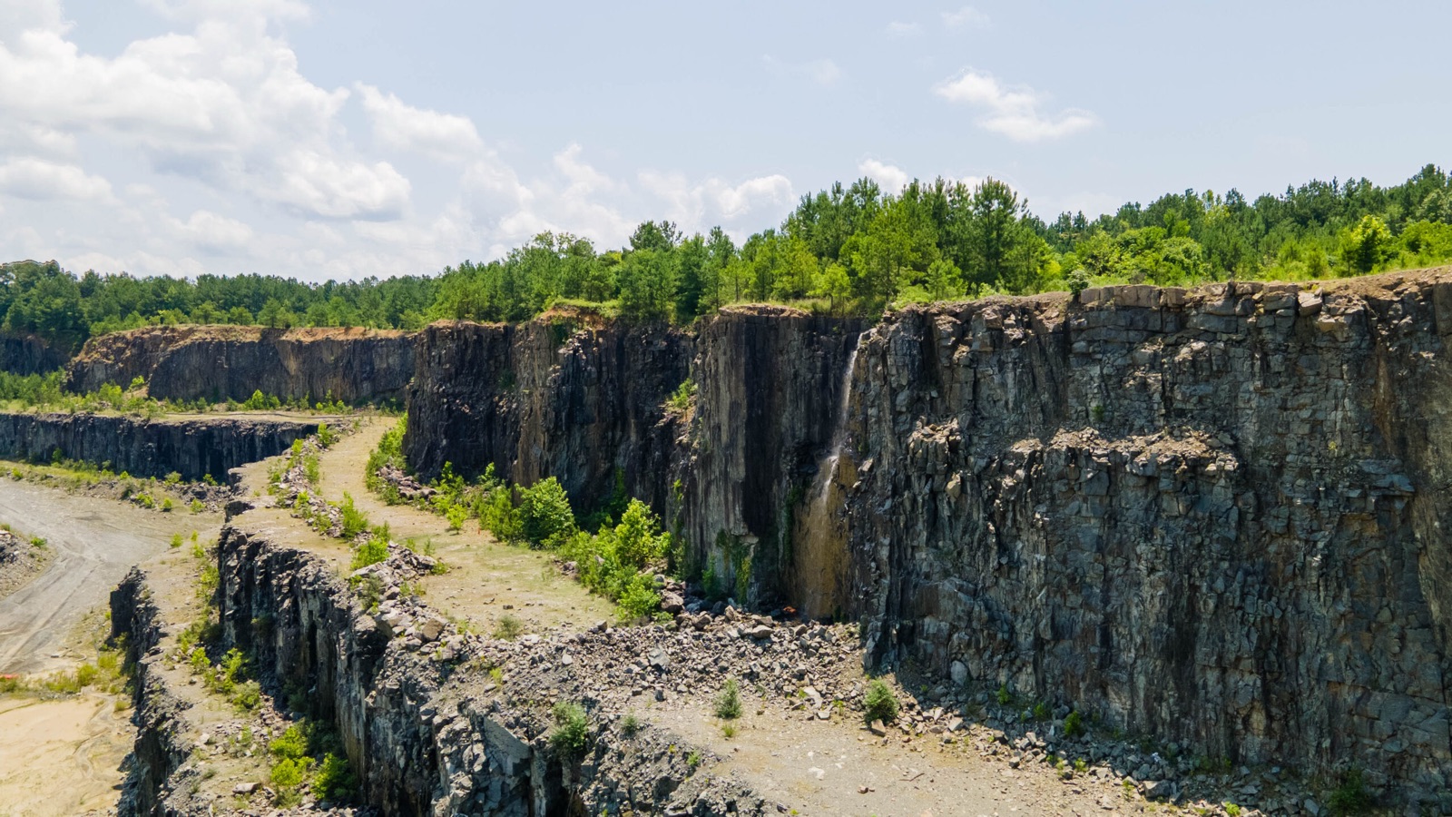 Benched rock walls at a Sunrock quarry with regrowth along the rim